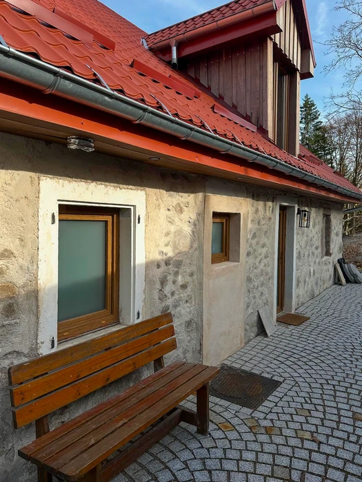 Façade en pierre naturelle apparente d'un bâtiment rénové, avec toiture en tuiles romanes rouge vif et chéneaux en zinc