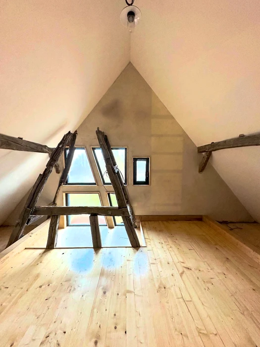 Comble aménagé avec plancher en lames de bois massif clair, murs en pente formant un toit à deux versants