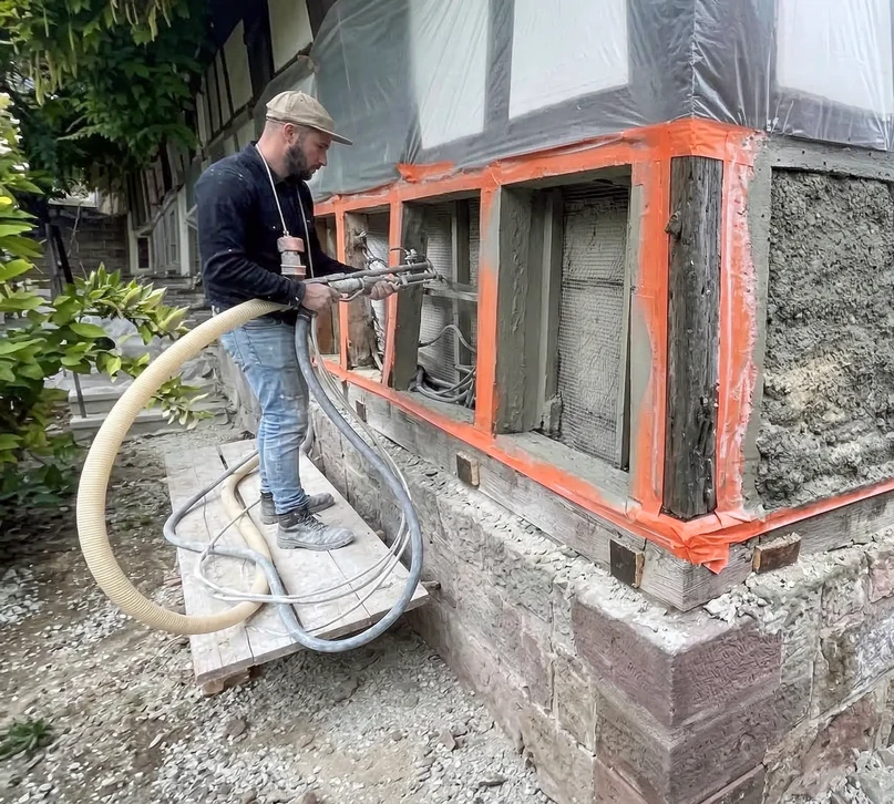 Ouvrier en salopette bleue installant des panneaux d'isolation thermique extérieure sur façade de maison en construction