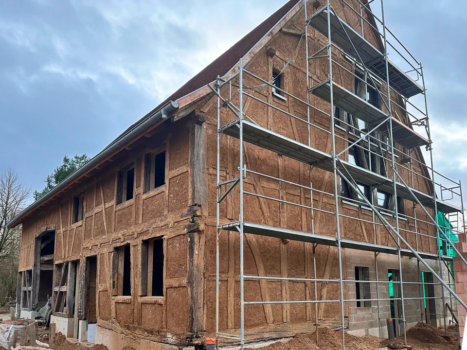 Ouvrier en équipement de protection appliquant un enduit ou traitement sur mur extérieur en briques beiges